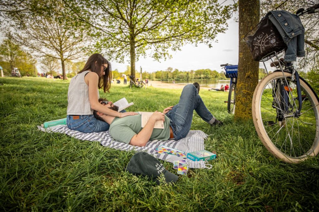 Couple d'amoureux en week-end à Rennes allongés sur l'herbe au bord de l'eau avec des vélos