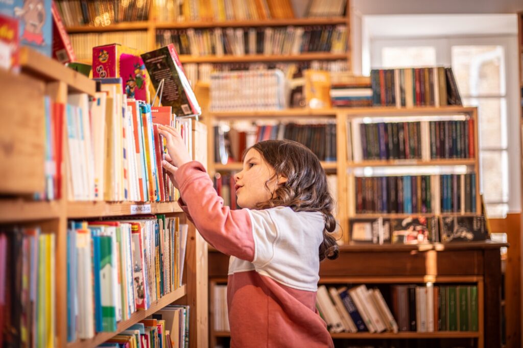 Une petite fille cherche un livre dans une librairie de Bécherel