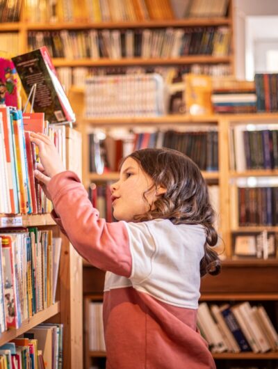 Une petite fille cherche un livre dans une librairie de Bécherel