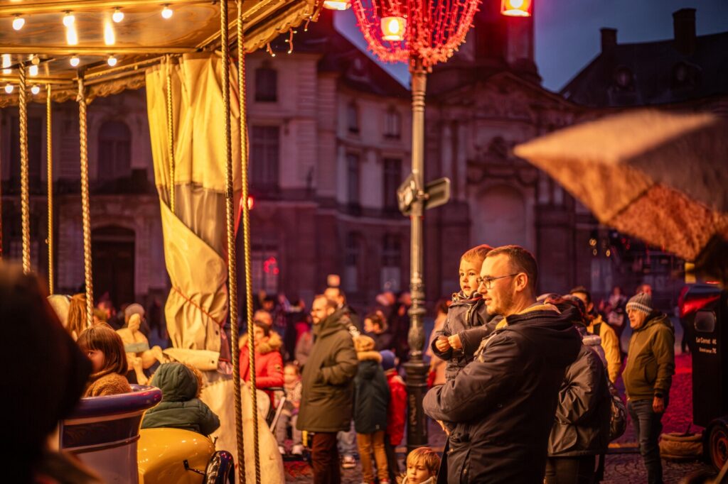 Un père avec son enfant regarde tourner le manège de la place de la Mairie