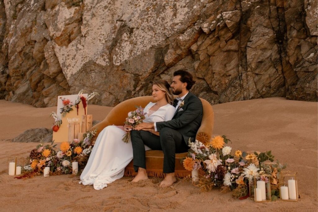 Couple assis sur un canapé sur la plage, entouré de fleurs et de bougies.